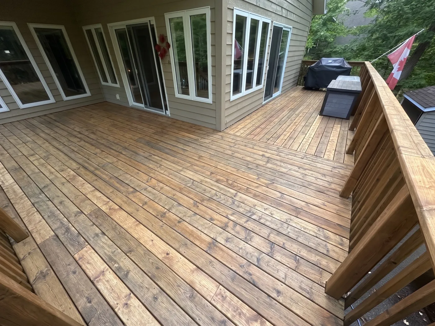A multi-level wood deck washed back to warm honey-brown, wrapping a Simcoe County home with a Canadian flag flying