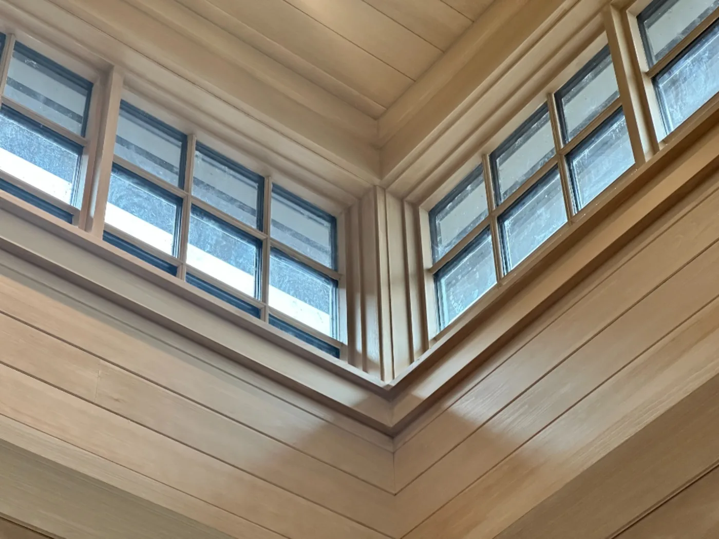 Before — Divided-lite clerestories in a cedar great room — hazy, hard-water-spotted glass detailed pane by pane until it reads crisp from the floor.