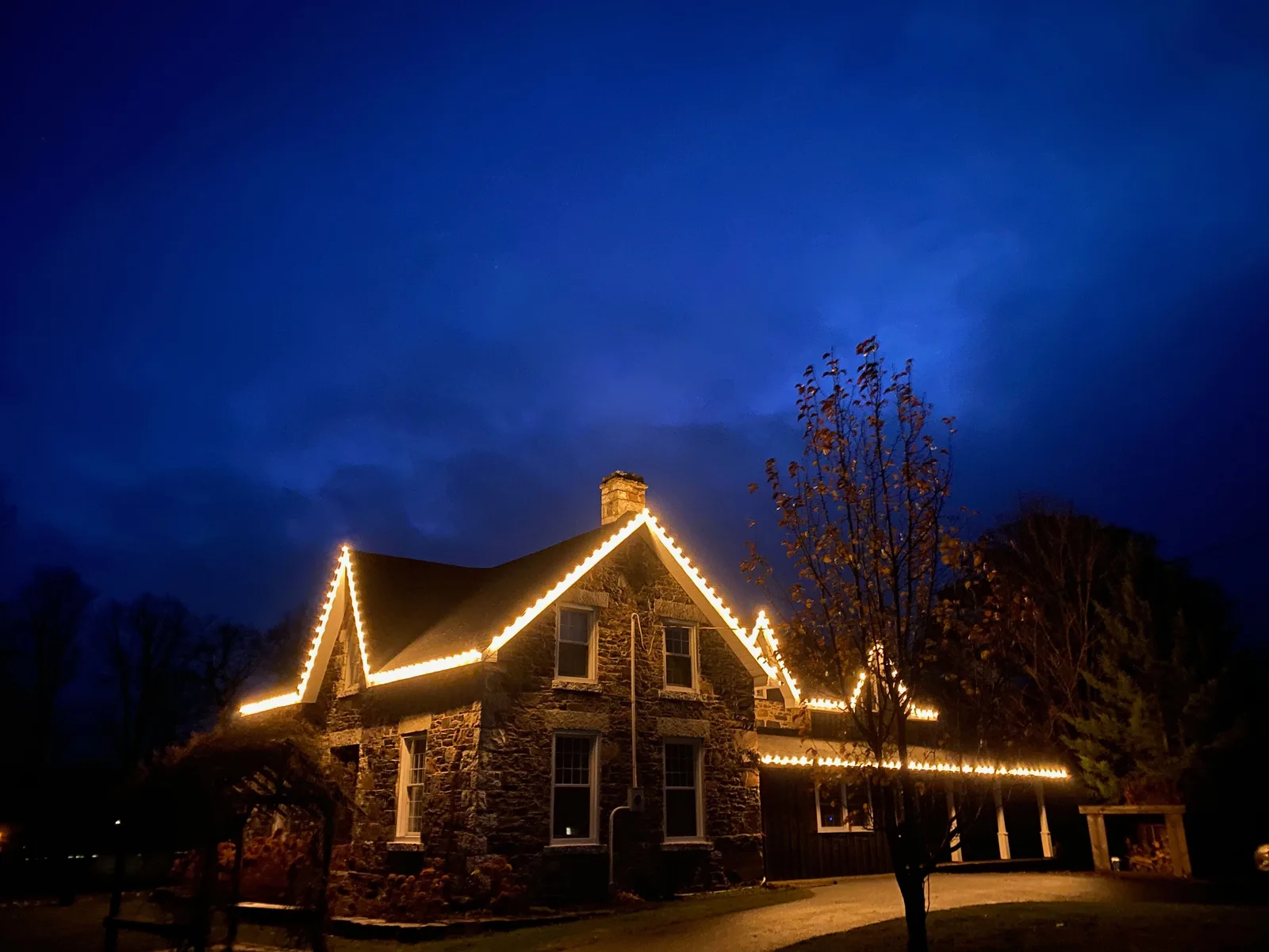 Professional Christmas light installation — Century Stone Farm · warm white on fieldstone at dusk