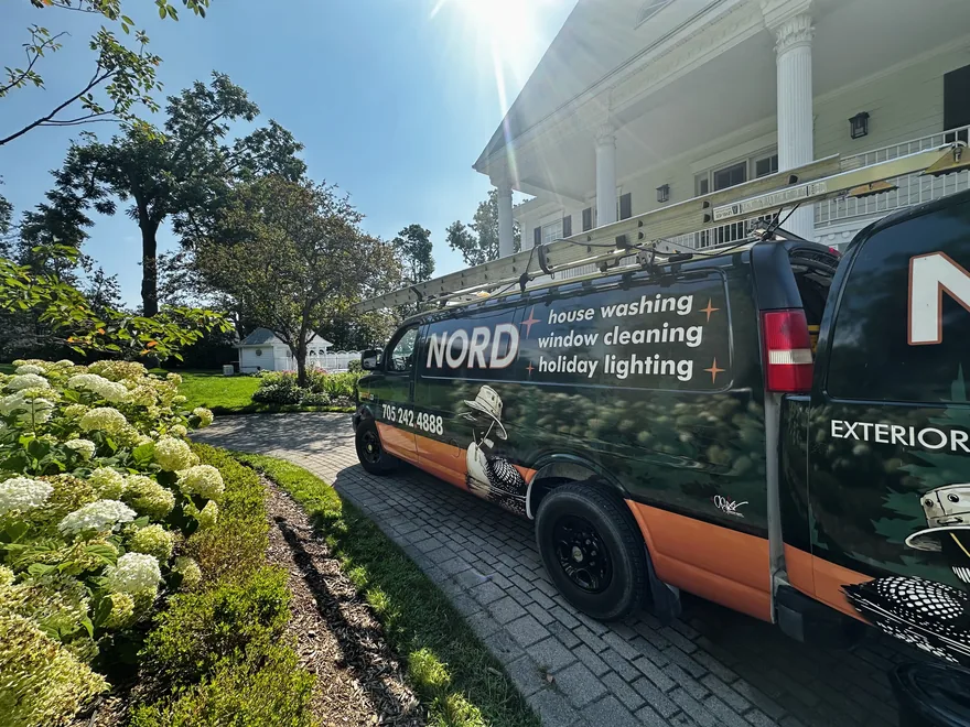 The Nord van — deep green wrap with the loon logo, house washing, window cleaning and holiday lighting listed on the side, ladders on the roof rack — parked on the drive of a white-columned Simcoe County home